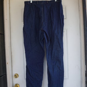 May include: Dark blue denim trousers hanging on a white hanger. The trousers are a solid colour with a classic five-pocket design. The trousers are hanging on a white door.