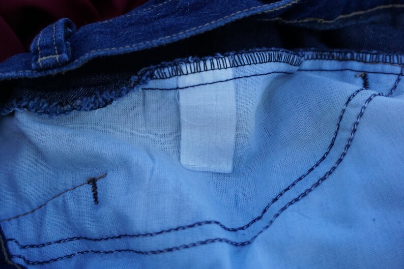 May include: Close-up of the inside of blue denim jeans. The image shows the light blue lining, the dark blue denim, and the stitching details. A white label is visible.