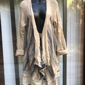 May include: A long-sleeved, beige cardigan with a blue and white striped pattern. The cardigan has a draped, asymmetrical hemline and a button closure.