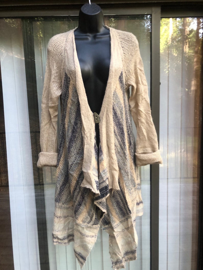 May include: A long-sleeved, beige cardigan with a blue and white striped pattern. The cardigan has a draped, asymmetrical hemline and a button closure.
