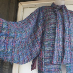 May include: A blue, purple, and red tweed jacket with a matching scarf. The jacket has a loose, oversized fit with wide sleeves. The fabric has a textured appearance with a mix of colors. The scarf is long and hangs down the front of the jacket.