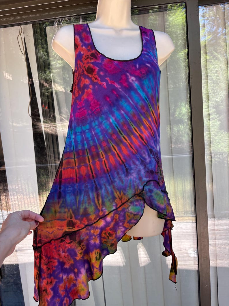 May include: A sleeveless tank top featuring a vibrant tie-dye pattern in shades of purple, blue, red, and orange. The garment has a scoop neckline and an asymmetrical, layered hemline with black stitched edges throughout the entire piece.