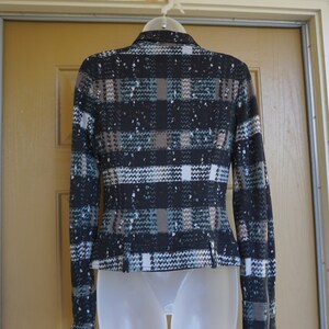 May include: A black, brown, and teal plaid jacket with a speckled pattern. The jacket has long sleeves, a zipper on the sleeve cuffs, and a tailored fit. It is displayed on a white mannequin form.