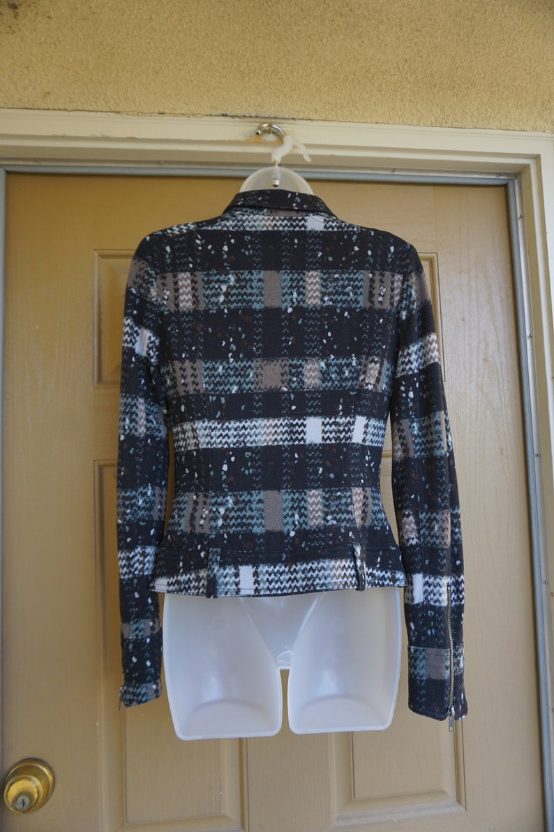 May include: A black, brown, and teal plaid jacket with a speckled pattern. The jacket has long sleeves, a zipper on the sleeve cuffs, and a tailored fit. It is displayed on a white mannequin form.