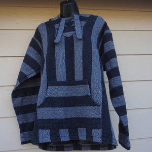 Puede incluir: Una sudadera con capucha Baja a rayas azules y grises con un bolsillo delantero y capucha. El jersey está hecho de una tela tejida y se muestra en un maniquí negro. La sudadera tiene un ajuste holgado y mangas largas.
