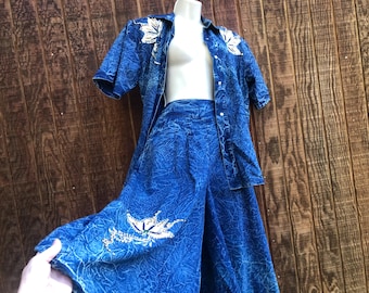 以下が含まれることがあります： 鮮やかなブルーの2ピースデニムセット。半袖のボタンダウンシャツとワイドレッグパンツで構成されています。白い葉の形の装飾が施されています。生地はテクスチャード加工が施されています。マネキンに着せられています。