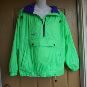 May include: Bright green anorak jacket with a purple-lined hood and a black zipper. The jacket has a front pocket with two black buttons and a drawstring at the bottom. The jacket is displayed on a mannequin.