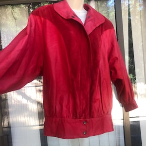 May include: A red jacket with a contrasting pink collar and shoulder panels. The jacket has long sleeves and a button closure at the waist. The jacket is made of a smooth, possibly satin-like material.