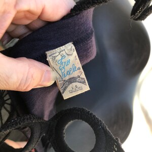 Op de afbeelding: Close-up van een donkerpaarse top met zwarte bandjes. Het label leest "Free People" in lichtblauw schrift. Het label geeft ook de maat Large en Made in India aan.