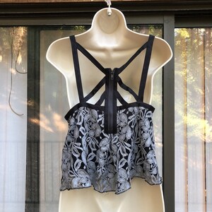 May include: A black and gray lace crop top with a black criss-cross strap design on the back. The top has a zipper closure in the back.