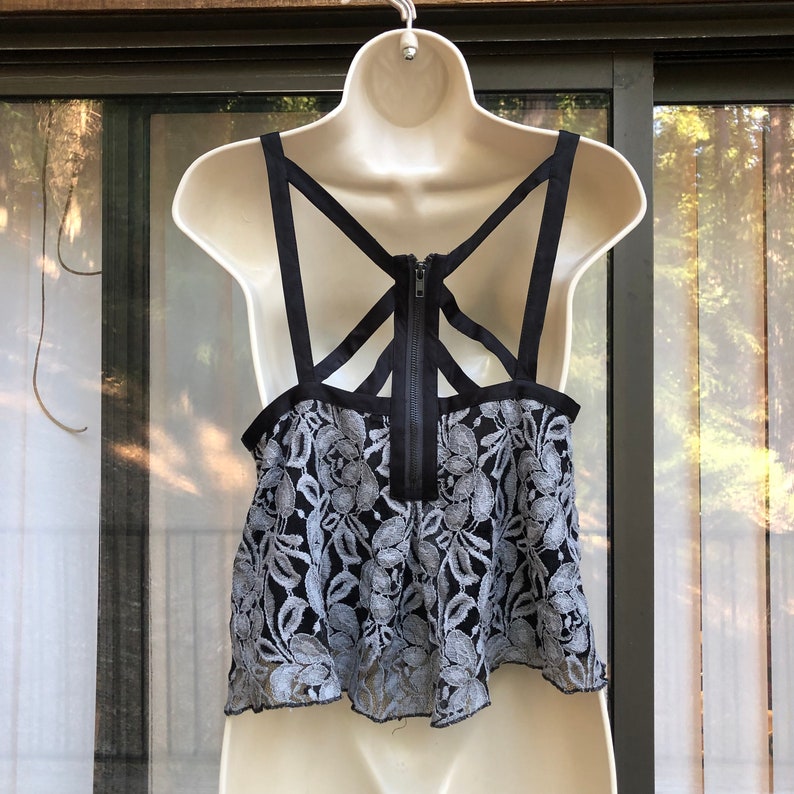 May include: A black and gray lace crop top with a black criss-cross strap design on the back. The top has a zipper closure in the back.