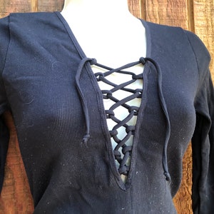 May include: A black long-sleeved shirt with a lace-up neckline. The shirt is made of a ribbed fabric.