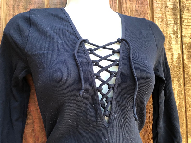 May include: A black long-sleeved shirt with a lace-up neckline. The shirt is made of a ribbed fabric.