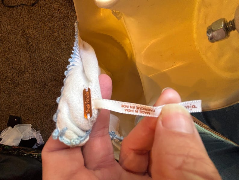 May include: A close-up of a white garment with light blue trim. The garment has a tag that reads "Free People". A white ribbon tag reads "MADE IN INDIA FABRIQUE EN INDE".