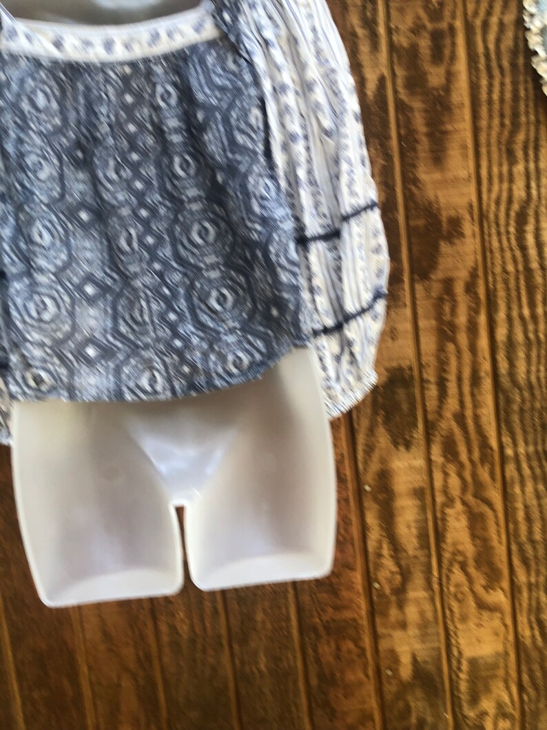 Puede incluir: Una blusa blanca y azul estampada con mangas largas. La blusa presenta un escote cuadrado y un dise&ntilde;o detallado en el corpi&ntilde;o. Las mangas tienen un estampado de rayas con detalles en azul oscuro. La prenda se exhibe en un maniqu&iacute; blanco.
