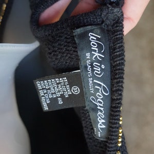 Pode incluir: Camisola preta com detalhes de contas douradas e uma etiqueta preta que diz "Work in Progress... by Sladys Bagley". A etiqueta tamb&eacute;m indica que a pe&ccedil;a &eacute; feita de 55% ramie e 45% algod&atilde;o. A etiqueta tamb&eacute;m indica que a pe&ccedil;a foi montada e acabada em Hong Kong, tricotada na China e tem um tamanho 3X.