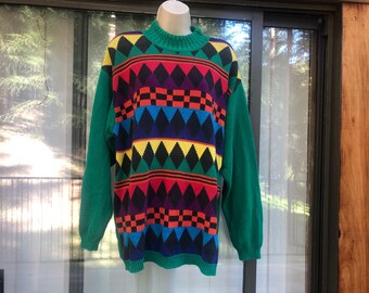 May include: A vintage sweater with a colorful geometric pattern. The sweater features a green turtleneck and sleeves, with a central design of diamonds, squares, and stripes in red, yellow, purple, and black. The sweater is displayed on a mannequin.