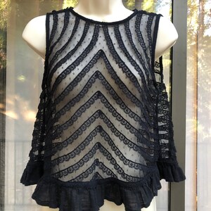 May include: Black lace sleeveless top with a chevron pattern and a ruffled hem.