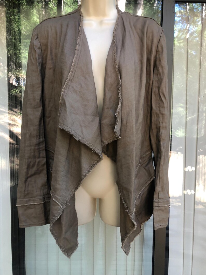 K&ouml;nnte beinhalten: Eine offene Jacke in Taupe mit einem drapierten Design. Die Jacke hat lange &Auml;rmel und ausgefranste Kanten am Kragen und an den Frontpartien. Der Stoff scheint ein leichter Leinenstoff oder ein &auml;hnliches Material zu sein.