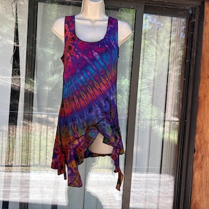 May include: A sleeveless tank top featuring a vibrant tie-dye pattern in shades of purple, blue, orange, and pink. The garment has a scoop neckline and an asymmetrical hemline with pointed edges, finished with black stitching along the seams.