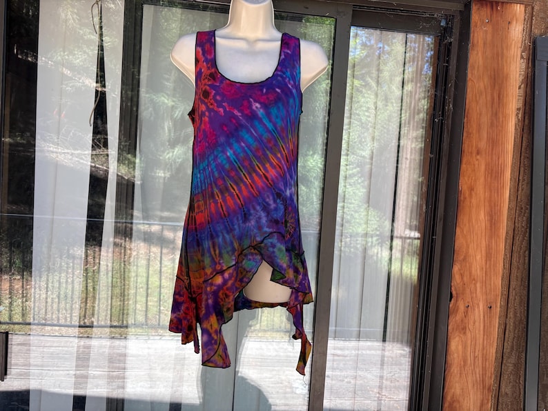 May include: A sleeveless tank top featuring a vibrant tie-dye pattern in shades of purple, blue, orange, and pink. The garment has a scoop neckline and an asymmetrical hemline with pointed edges, finished with black stitching along the seams.