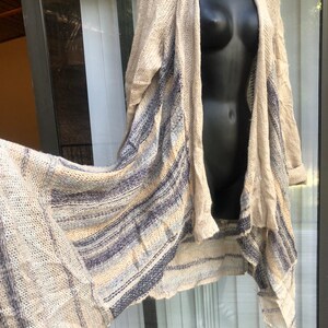 May include: A long, beige cardigan with blue and white stripes. The cardigan is open in the front and has a draped, asymmetrical hem.