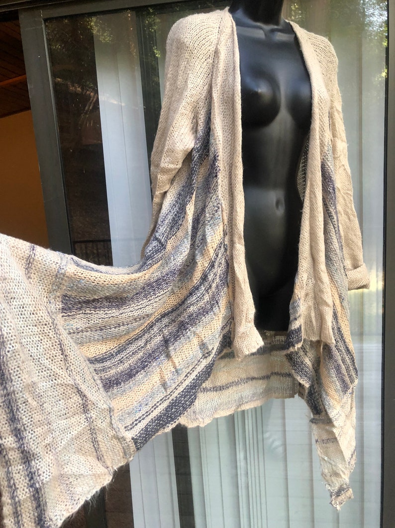May include: A long, beige cardigan with blue and white stripes. The cardigan is open in the front and has a draped, asymmetrical hem.