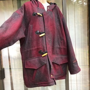 May include: A hooded, burgundy and black plaid duffel coat with wooden toggles and large front pockets. The coat has a classic design and is made of a thick, warm material, perfect for cold weather.