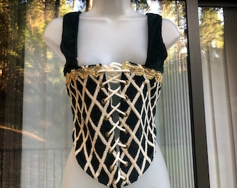 May include: A dark green corset with a diamond pattern, cream-colored lacing, and gold trim. The corset has wide shoulder straps and a lace-up front. The garment is displayed on a mannequin.