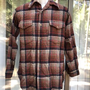 May include: A long-sleeved, button-down flannel shirt in a plaid pattern of brown, red, and navy blue. The shirt has two chest pockets and a collared neckline. The fabric appears to be a thick, warm material.