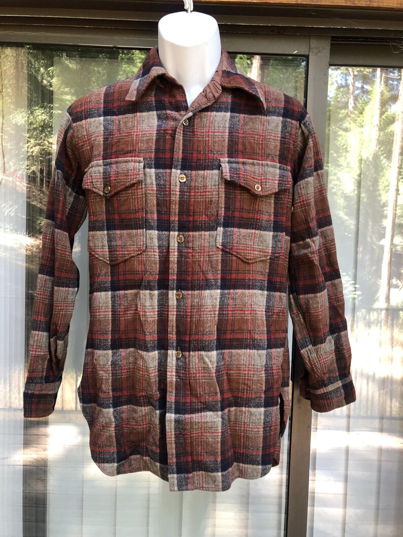 May include: A long-sleeved, button-down flannel shirt in a plaid pattern of brown, red, and navy blue. The shirt has two chest pockets and a collared neckline. The fabric appears to be a thick, warm material.