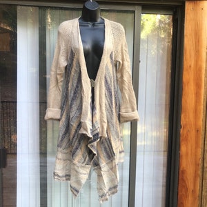 May include: A long, beige cardigan with a blue and white striped pattern. The cardigan has a draped, asymmetrical hemline and a V-neck.
