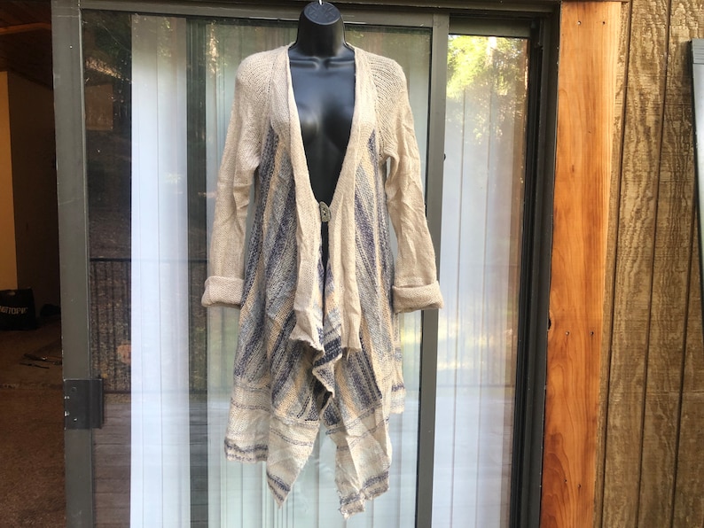 May include: A long, beige cardigan with a blue and white striped pattern. The cardigan has a draped, asymmetrical hemline and a V-neck.