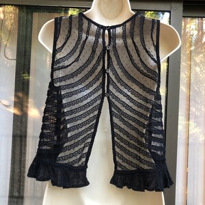 May include: Black lace sleeveless vest with a button-up back and a ruffled hem.