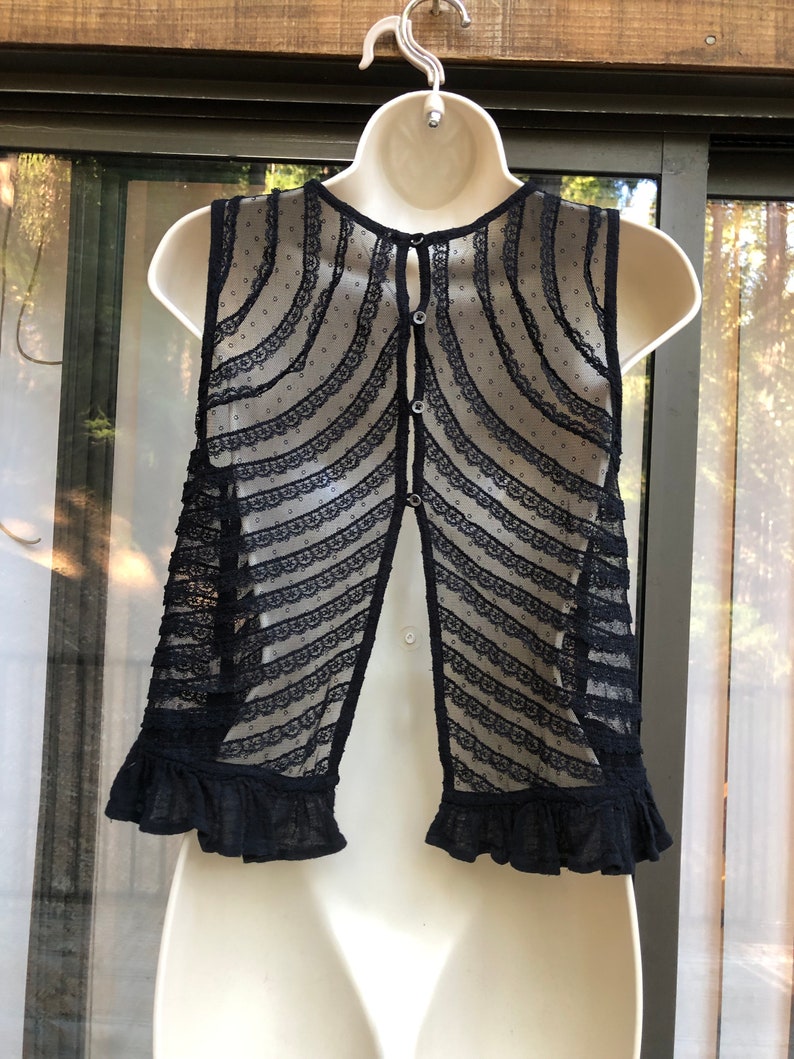 May include: Black lace sleeveless vest with a button-up back and a ruffled hem.