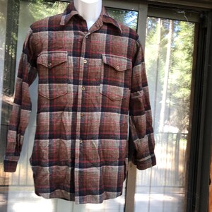 May include: A long-sleeved, button-down shirt in a plaid pattern of brown, red, and navy blue. The shirt has two chest pockets and is displayed on a mannequin. The fabric appears to be a heavier weight, suitable for cooler weather.