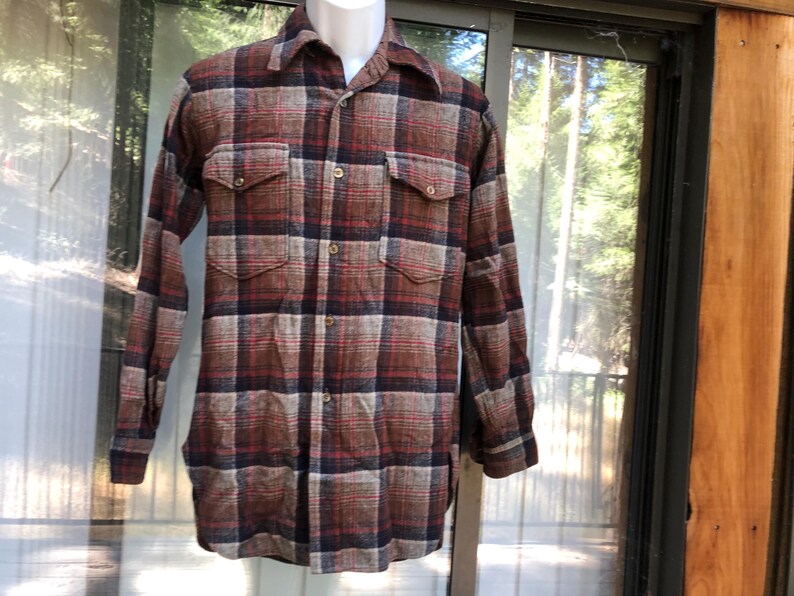 May include: A long-sleeved, button-down shirt in a plaid pattern of brown, red, and navy blue. The shirt has two chest pockets and is displayed on a mannequin. The fabric appears to be a heavier weight, suitable for cooler weather.