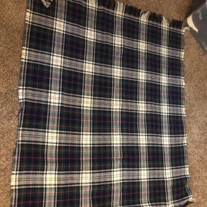 May include: A white, green, and black plaid throw blanket with fringed edges.