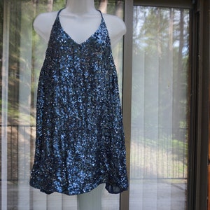 K&ouml;nnte beinhalten: Ein marineblaues Paillettenkleid mit Neckholder-Ausschnitt und V-Ausschnitt. Das Kleid ist &auml;rmellos und locker fallend. Die Pailletten verleihen dem Kleid ein schimmerndes Aussehen. Das Kleid wird auf einer wei&szlig;en Schaufensterpuppe pr&auml;sentiert.