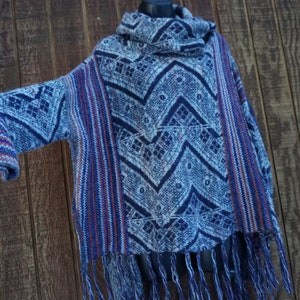 May include: A blue, white, and red patterned poncho with a cowl neck and fringe. The poncho features a geometric design and is made of a woven fabric. The sleeves have a striped pattern in red, white, and blue.