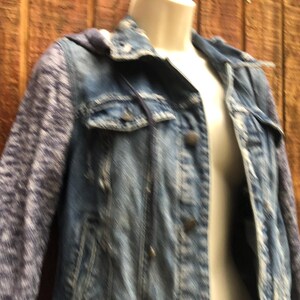 May include: A blue denim jacket with a hood and patterned sleeves. The jacket has a button-up front, two chest pockets, and a classic collar. The sleeves are a patterned knit fabric.