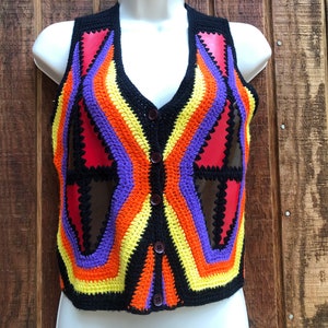 May include: A colorful crocheted vest with a geometric pattern in shades of red, orange, yellow, purple, and black. The vest has a button closure and is sleeveless.