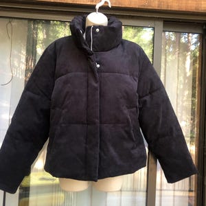 May include: A dark navy blue puffer jacket with a high collar and button closure. The jacket has a quilted design and long sleeves. The jacket is displayed on a mannequin.
