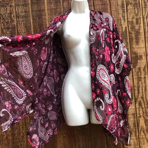 Puede incluir: Un kimono de gasa con estampado de paisley en color burdeos y rosa con borde festoneado.
