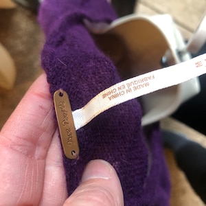 May include: A close-up of a purple garment with a tag that says "free people". A white tag with the text "MADE IN CHINA" and "FABRIQUE EN CHINE" is also visible. The garment is held by a person.