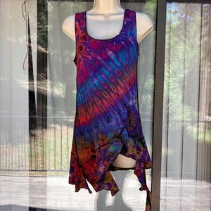 May include: A sleeveless tunic top featuring a vibrant tie-dye pattern in shades of purple, blue, orange, and pink. The garment has a scoop neckline, black stitched seams, and an asymmetrical hemline with multiple points that drape unevenly.