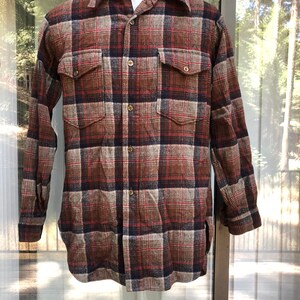 May include: A long-sleeved, button-down shirt in a plaid pattern. The shirt features a color palette of brown, red, and navy blue. It has two chest pockets and a classic collar. The shirt is displayed on a mannequin.