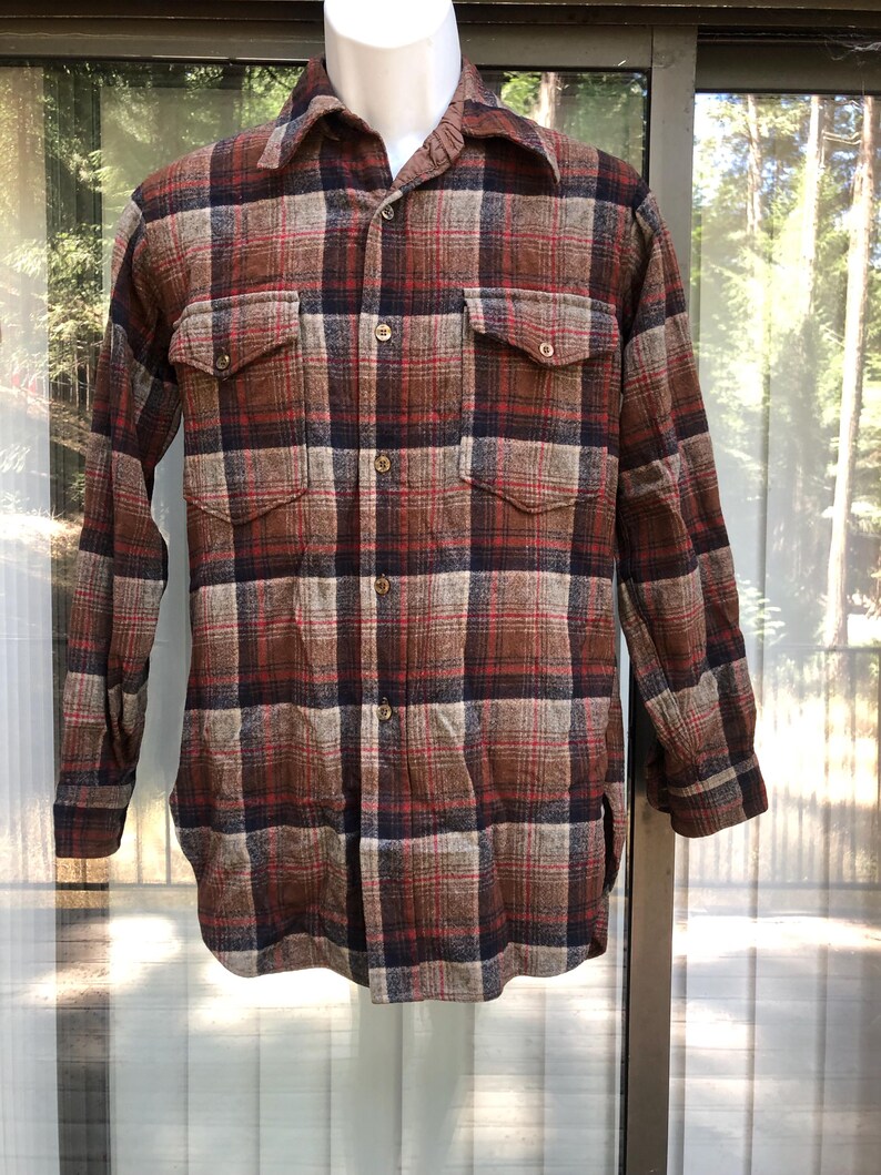 May include: A long-sleeved, button-down shirt in a plaid pattern. The shirt features a color palette of brown, red, and navy blue. It has two chest pockets and a classic collar. The shirt is displayed on a mannequin.