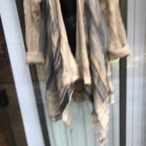 May include: A beige cardigan with a black and white geometric pattern. The cardigan has a draped front and a long, flowing style.