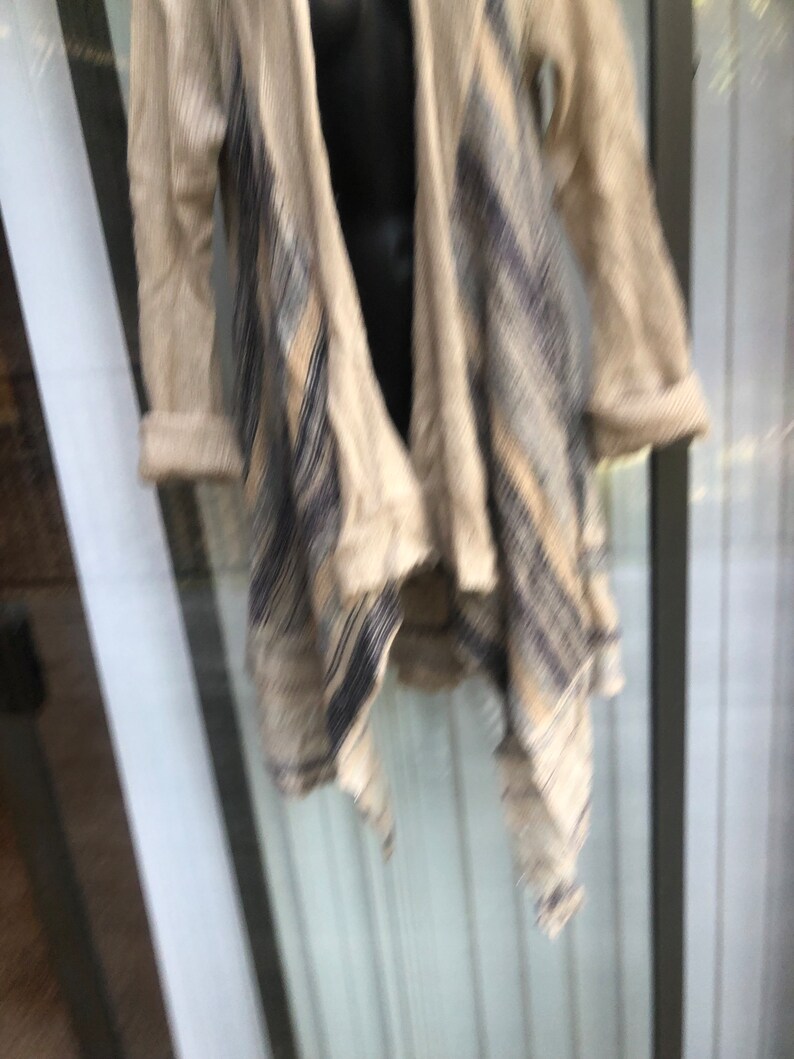 May include: A beige cardigan with a black and white geometric pattern. The cardigan has a draped front and a long, flowing style.